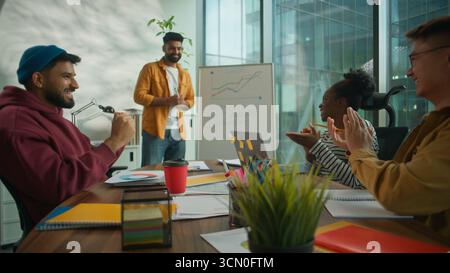 Presentazione di successo della startup in un ufficio di coworking informale e multiculturale, un team aziendale informale e diversificato che applaude il leader maschile mostrando il grafico di crescita Foto Stock