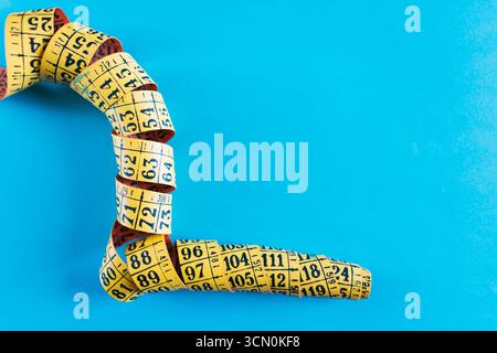 Un nastro di misurazione giallo arrotolato su sfondo blu. Foto Stock