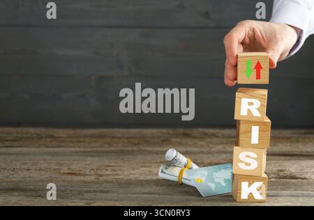 Rischio aziendale. Uomo che mette un cubo di legno con frecce sulla pila, carta di credito e denaro sul tavolo Foto Stock