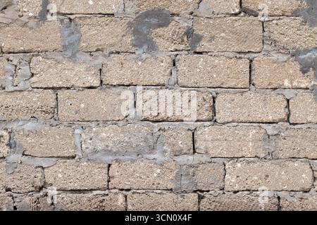 Vista ravvicinata di un muro di mattoni ruvidi che mostra un aspetto ruvido, invecchiato con Malta visibile e irregolarità naturali, perfetto per l'architettura o. Foto Stock