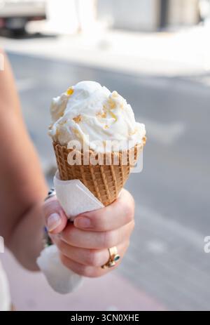 Rethymno, Creta, Grecia. Una donna che tiene una grande tazza di gelato in un cono di waffle. Il gelato ha un sapore di torta all'arancia Foto Stock