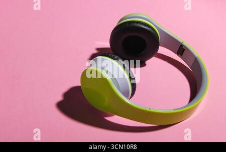 Eleganti cuffie stereo wireless con ombra su sfondo rosa pastello. Amante della musica Foto Stock