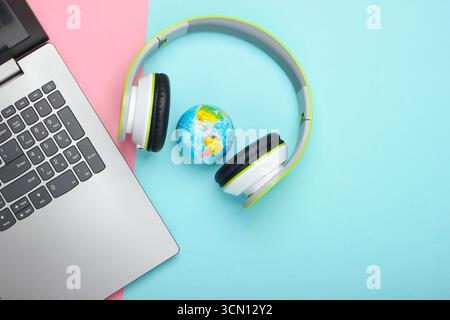 Rete globale, Internet. Canzone World Music. Laptop, cuffie stereo e globo su sfondo rosa blu pastello. Vista dall'alto Foto Stock