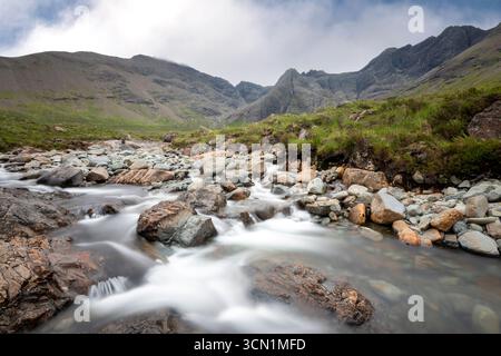 Le Fairy Pools di Skye in Scozia risplendono di luce pallida e acque lisce che avvolgono rocce muschiate mentre le ombre delle montagne donano una calma cristallina e cristallina. Foto Stock