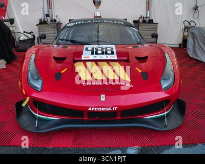 Vista frontale di una Ferrari 488 da corsa rossa - Una vista frontale simmetrica di una Ferrari 488 GT rossa con un trofeo sul tetto, parcheggiata all'interno di un professionista Foto Stock