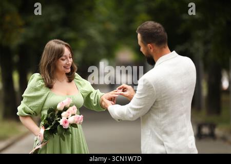 Fare una proposta di matrimonio. Uomo che mette l'anello di fidanzamento al dito della sua ragazza all'aperto Foto Stock