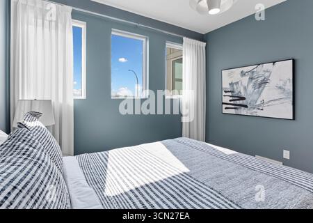 Camera da letto con letto bianco e pareti blu. Il letto è coperto da un piumone a righe Foto Stock