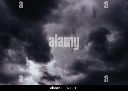 Un cielo tempestoso pieno di nuvole minacciose, scure e pesanti e basse, che creano una scena drammatica. Foto mostruosa di un cielo grigio cupo pieno di nuvole vorticose e tempeste Foto Stock
