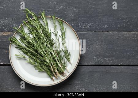 Piatto con ramoscelli di rosmarino freschi su fondo in legno nero Foto Stock