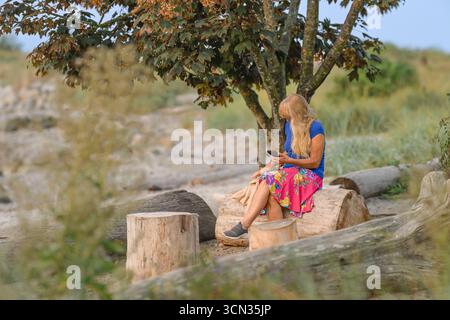 donna che guarda il telefono seduto sul tronco sulla spiaggia deserta Foto Stock
