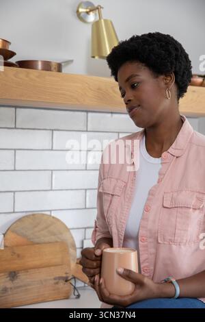 Donna afroamericana di medie dimensioni con tazza in ceramica vicino ai taglieri in cucina, spazio copia Foto Stock