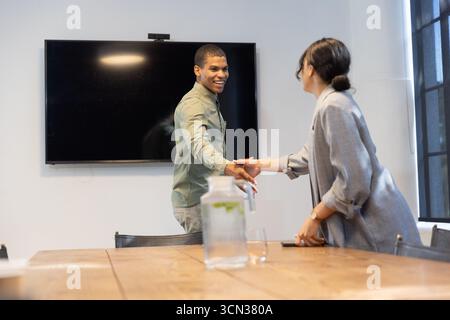 Diversi colleghi che stringono la mano sul tavolo da conferenza nella sala riunioni con pitche e smartphone Foto Stock