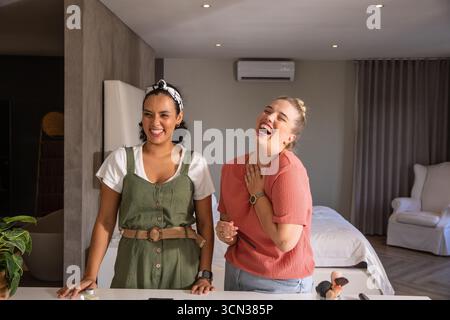 Diverse amiche che ridono mentre usano i pennelli per il trucco sul ripiano della camera da letto Foto Stock