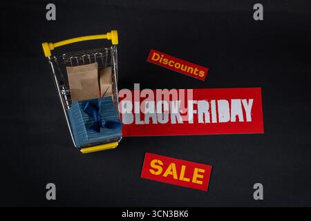 Carrello della spesa in miniatura pieno di regali su sfondo nero con sconti e etichette di vendita Foto Stock