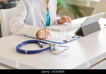 Medico professionista, medico o infermiere scrittura a mano negli appunti, digitazione su tastiera, lavoro alla scrivania Foto Stock