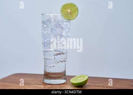 Un rinfrescante bicchiere di bibita fredda o acqua tonica con cubetti di ghiaccio e una fetta di lime fresca. Un concetto minimalista per un drink estivo, un cocktail o un sano re Foto Stock