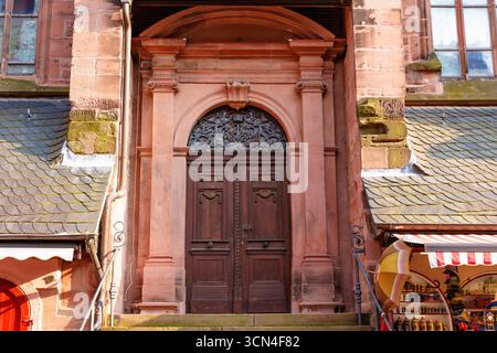 Heidelberg, Germania - 8 giugno 2025: Porta ornata in legno con dettagliate incisioni e arcata in pietra, adagiata su un muro testurizzato con scale che conducono Foto Stock