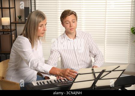 Tutore che insegna all'uomo a suonare il pianoforte al chiuso Foto Stock