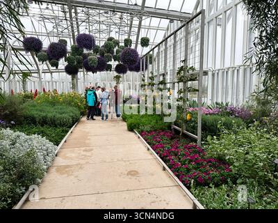 Kennett Square, Pennsylvania, USA - 15 aprile 2025: Visitatori all'interno della serra di Longwood Gardens circondata da piante e fiori vivaci. Foto Stock