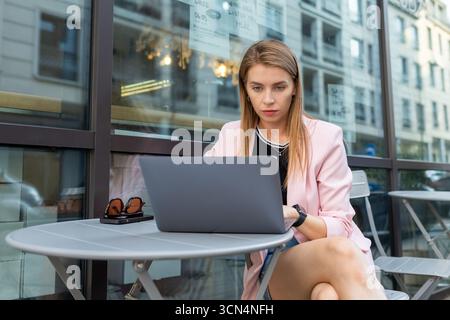 Una donna professionista è impegnata con un computer portatile al tavolo del bar Foto Stock