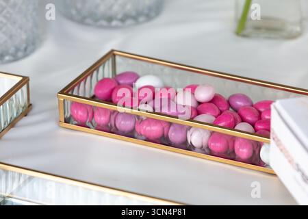 Mandorle zuccherate che riempiono un contenitore di vetro con bordo dorato seduto su un tavolo bianco Foto Stock