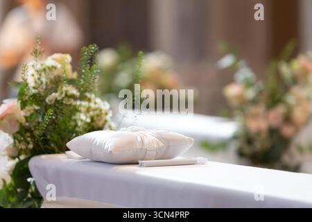 Cuscino di raso bianco e penna collocati sull'altare, in attesa delle fedi nuziali durante la cerimonia della chiesa Foto Stock
