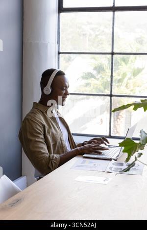 Uomo afroamericano medio adulto che indossa le cuffie scrivendo sul laptop, spazio per copiare Foto Stock