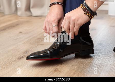 Primo piano di un uomo d'affari che lega i lacci delle sue eleganti scarpe in pelle nera, preparandosi per un'occasione speciale Foto Stock