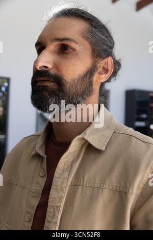 Uomo indiano medio adulto in piedi in un moderno studio che guarda a sinistra, con travi a soffitto in legno Foto Stock