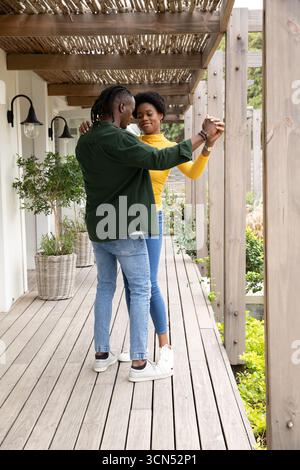 Coppia afroamericana che si tiene per mano, ballando su un ponte di legno sotto pergola con applique a lanterna Foto Stock