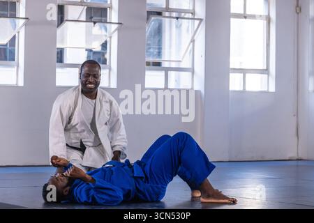 Istruttore afro-americano che guida gli studenti che praticano il dojo su tappeti che indossano gis Foto Stock
