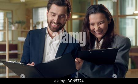 Uomini d'affari contenti multietnici colleghi discutono rapporti documenti in ufficio uomo d'affari caucasico donna d'affari coreana partner manager che ridono Foto Stock