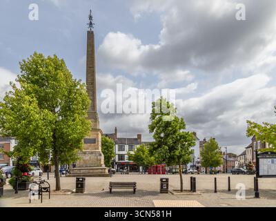 L'obelisco di Ripon nella piazza del mercato, North Yorkshire, un monumento classificato Grade i costruito nel 1702, circondato da alberi, panchine, negozi e cabine telefoniche Foto Stock
