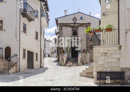 Vista di una pittoresca cappella in pietra annidata tra edifici imbiancati su strade acciottolate sotto un cielo limpido, Pescocostanzo, Abruzzo, Italia. Foto Stock