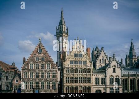 Vista del Korenlei a Gand, Belgio, con l'iconica torre dell'orologio al centro e le tradizionali case belghe parzialmente visibili sotto un cielo blu Foto Stock