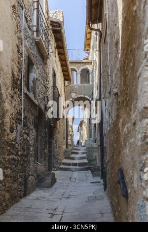 Vista di uno stretto sentiero in pietra che si snoda attraverso edifici antichi sotto un arco, dove la luce illumina una figura, Castelvecchio Calvisio, Abruzzo, Italia. Foto Stock