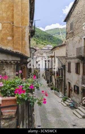 Veduta di stradine strette fiancheggiate da vecchi edifici, fioriere e lussureggianti colline verdi che si estendono verso il cielo, Scanno, Abruzzo, Italia. Foto Stock