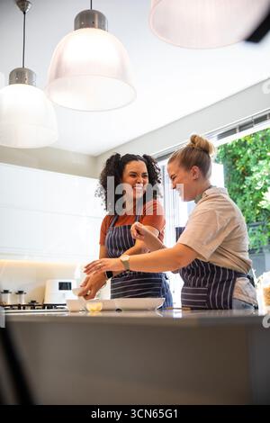 Diverse amiche che indossano grembiuli a righe che mescolano le uova nel recipiente di miscelazione in cucina Foto Stock