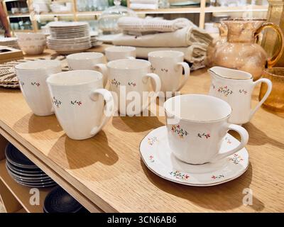 Le tazze da tè in ceramica bianca con motivi floreali sono splendidamente disposte su un tavolo di legno, creando un'atmosfera invitante perfetta per riunioni o tè Foto Stock