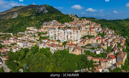 Veduta aerea che mostra lo storico villaggio di Pietravairano annidato su un rigoglioso pendio di montagna verde con architettura tradizionale e un vecchio castello. Foto Stock