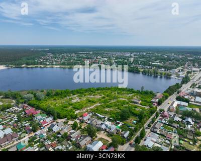 Un'ampia vista aerea di Gus Khrustalny, che mostra case residenziali lungo la riva di un grande lago con campi verdi e una fitta foresta all'orizzonte. Foto Stock