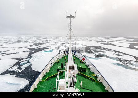 Nave rompighiaccio che naviga nel Mar Artico Ice Svalbard Norvegia // SVALBARD E JAN MAYEN - una nave rompighiaccio naviga attraverso una vasta distesa di ghiaccio marino artico. La prua della nave taglia attraverso l'oceano ghiacciato, circondato da numerosi banchi di ghiaccio di varie dimensioni. Il paesaggio circostante è dominato da ghiaccio bianco e acqua scura e aperta, sotto un cielo pesantemente coperto. Questa scena cattura le condizioni difficili affrontate dalle imbarcazioni che operano in regioni polari. L'arcipelago delle Svalbard, situato nell'Oceano Artico, è noto per i suoi spettacolari ghiacciai, le montagne e l'abbondante fauna selvatica, che lo rendono un ottimo destina Foto Stock
