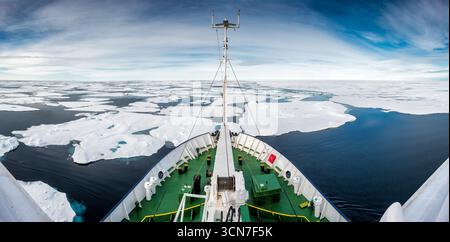 Ice rafforzò la nave della spedizione spingendo attraverso Sea Ice a nord delle Svalbard // SVALBARD E JAN MAYEN - una nave da spedizione rinforzata dal ghiaccio naviga attraverso il ghiaccio marino a nord delle Svalbard. La nave, progettata per l'esplorazione polare, spinge attraverso acque frigide punteggiate da banchi di ghiaccio sotto un cielo ampio e nuvoloso. Questa regione è nota per le sue difficili condizioni artiche ed è un percorso comune per spedizioni scientifiche e avventurose. Lo scafo rinforzato della nave consente di attraversare mari ghiacciati, facilitando l'accesso a ambienti polari remoti. Foto Stock
