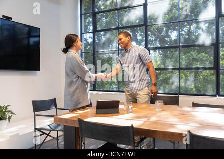 Diversi colleghi che stringono la mano sul tavolo da conferenza in legno nella sala riunioni dell'ufficio, tablet Foto Stock