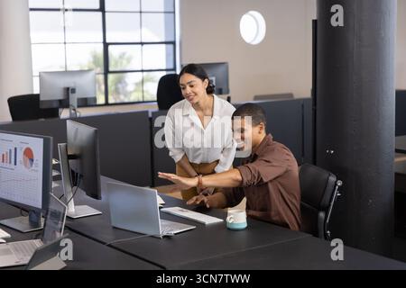 I colleghi afroamericani che collaborano alle classifiche presso la moderna scrivania dell'ufficio con computer portatile e tazza da caffè Foto Stock