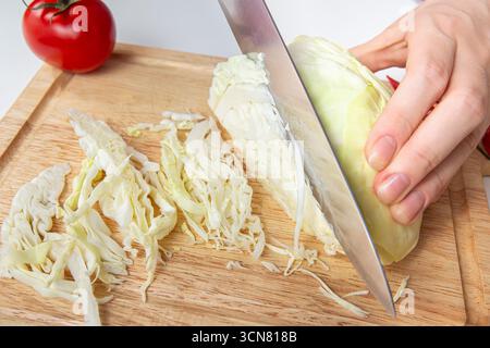 Primo piano di un taglio a mano di cavolo fresco con un coltello affilato su un tagliere di legno, preparazione alimentare, cottura sana Foto Stock