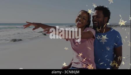 Spalmare le braccia sorridenti seduti sulla spiaggia di sabbia in t-shirt, con sovrapposizioni grafiche a forma di stella Foto Stock