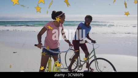 Coppia sorridente che indossa abiti estivi in sella alle biciclette da crociera in spiaggia, con grafica a stella dorata Foto Stock