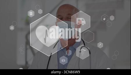 Medico anziano in piedi indossando maschera chirurgica, stetoscopio in clinica, con icone di salute fluttuanti Foto Stock