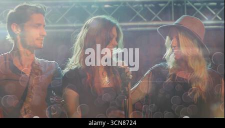 Banda di jamming che suona sotto capriata metallica, con chitarra elettrica, microfono, collana e impianto di illuminazione Foto Stock